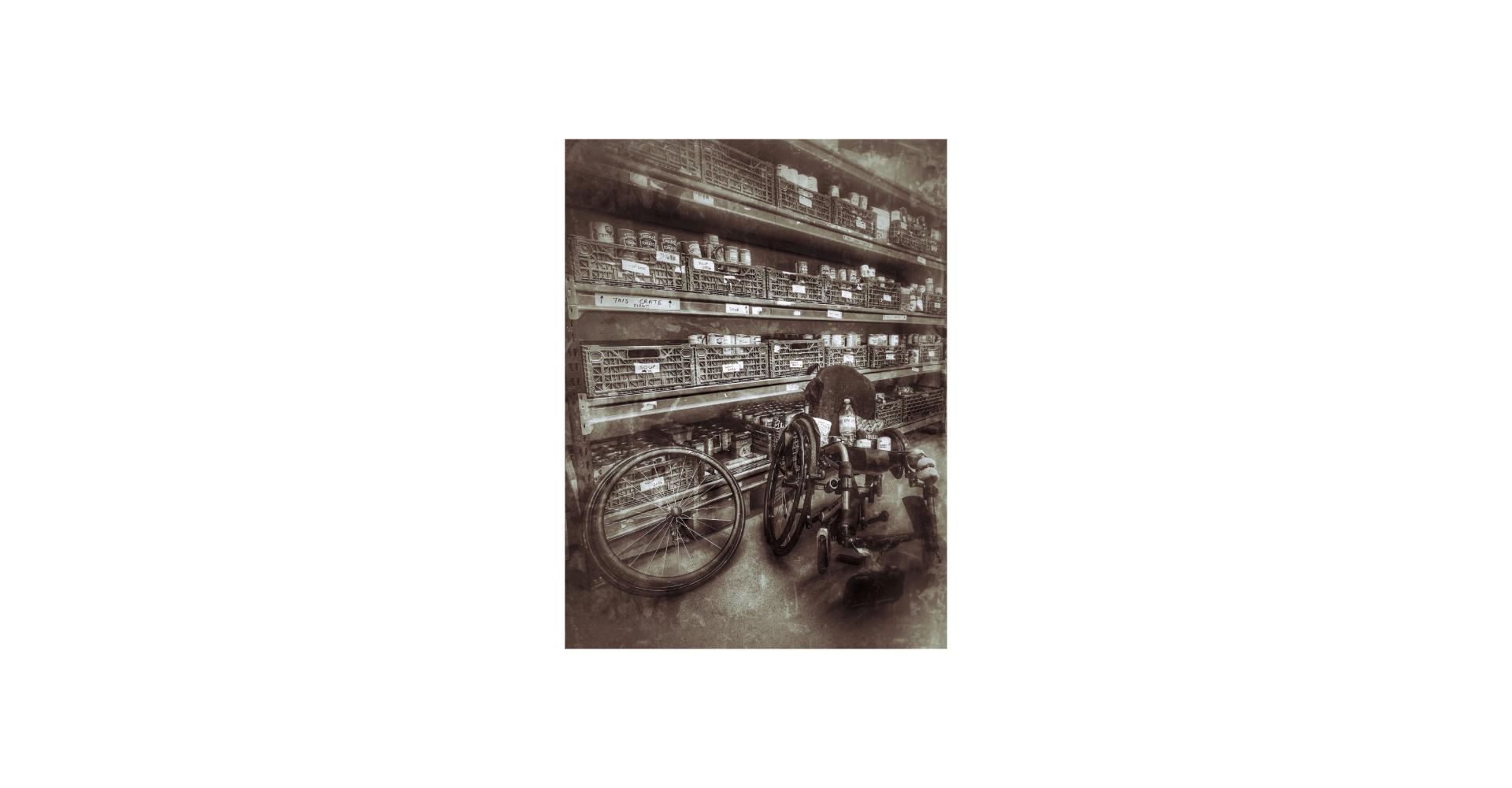 Broken wheel chair in front of shelves of tinned food